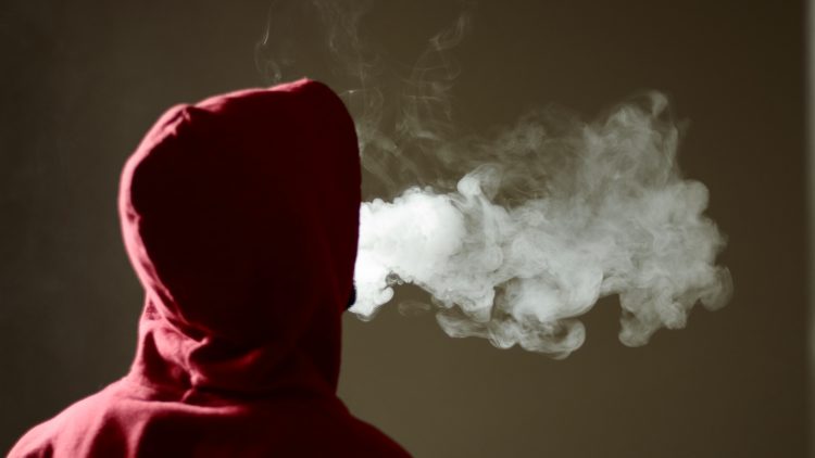 Youth in hood expelling vape smoke.Image Credit: iStock
