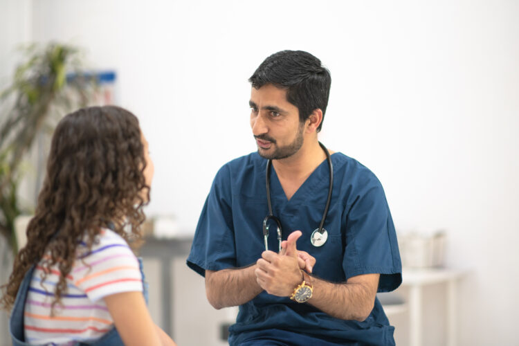 A male nurse of Indian ethnicity explains something to a young girl in the doctor's office. Photo Credit: iStock