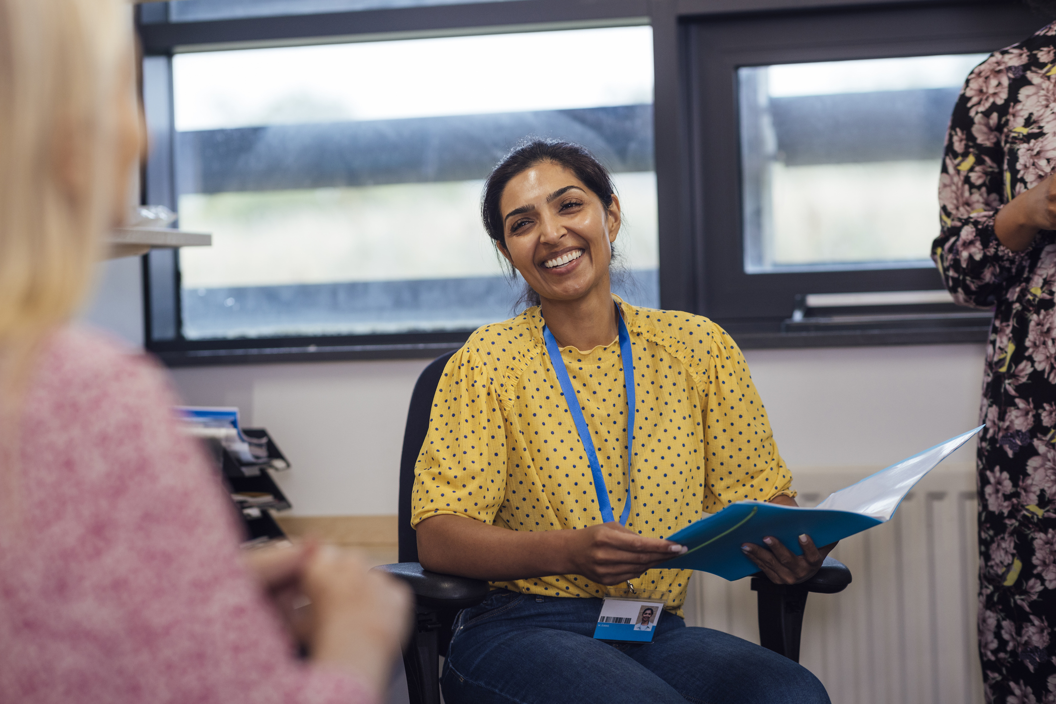 An over-the-shoulder shot of a teacher smiling in a meeting, wearing smart-casual clothing. The teachers are sitting in an office within a secondary school in Gateshead, England.