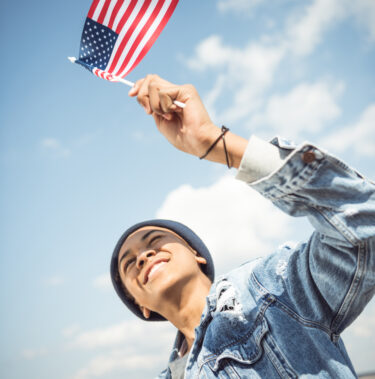 smiling african american teenager waving american flag, hipster style concept