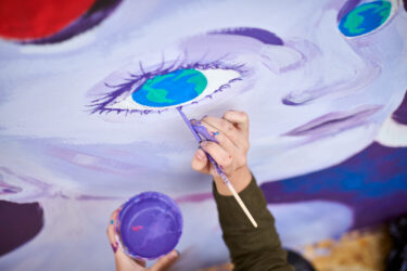 Female painter draws picture with paintbrush on canvas for outdoor street exhibition, close up above top view of female artist apply brushstrokes to canvas, symphony of art creativity