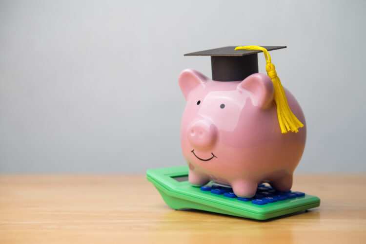 Piggy bank wear mortarboard and green calculator on wooden table with white wall background copy space. Private student loan, student debt, repayment plan, expense , money management, scholarship and so on concept