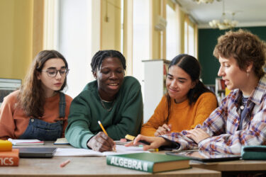 Group of students working on an algebra project in classroom setting, engaging in collaborative learning while sitting around table and sharing ideas on assignment