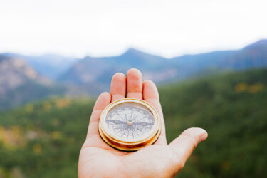 Hiker holding a compass, navigating through a stunning mountain landscape, searching for the right path on an adventurous journey