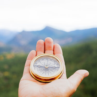 Hiker holding a compass, navigating through a stunning mountain landscape, searching for the right path on an adventurous journey
