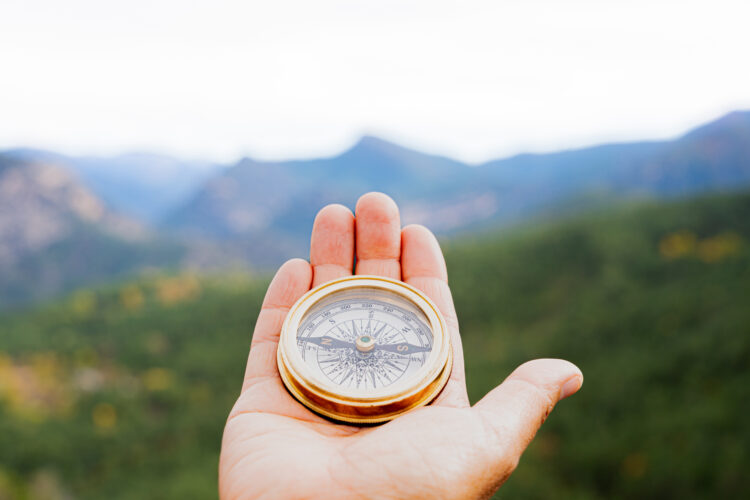 Hiker holding a compass, navigating through a stunning mountain landscape, searching for the right path on an adventurous journey