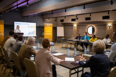 A large group of business conference participants listening to a young woman's speech in a luxury hotel's conference room