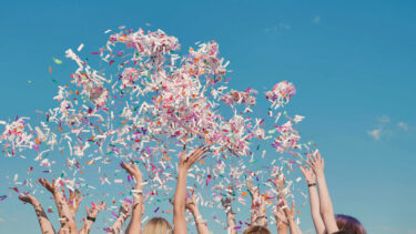 Group of high school students throwing colorful confetti in the air, celebrating graduation on a sunny day
