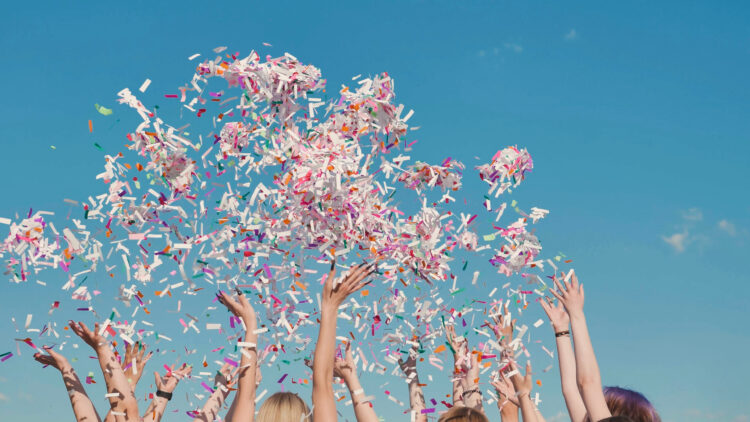 Group of high school students throwing colorful confetti in the air, celebrating graduation on a sunny day